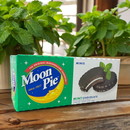 A box of Mini MoonPie mint chocolate cookies placed on a wooden surface with mint plants in the background.